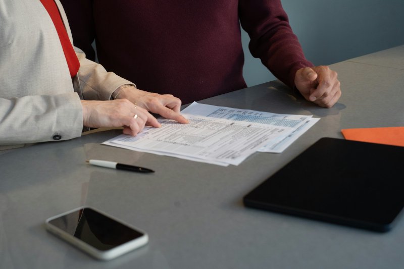Two people seated at a desk reviewing printed documents alongside a tablet and smartphone