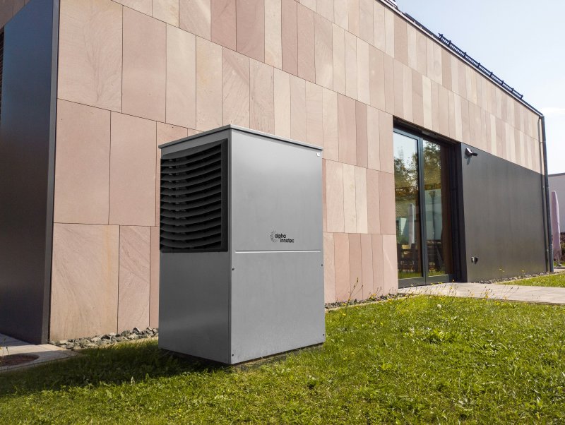 Gray residential outdoor condenser unit set on grass beside a modern stone-faced home