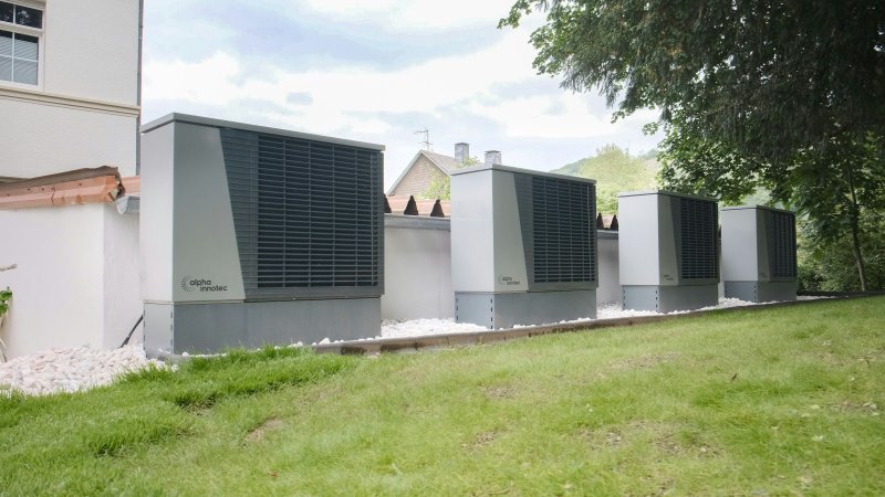 Row of outdoor air conditioning condenser units on concrete pads beside a residential building