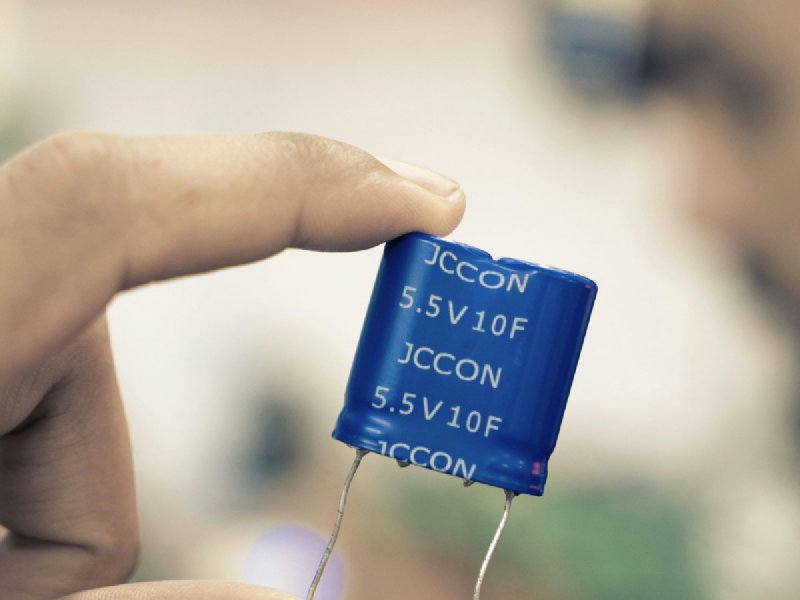 Hand holding a cylindrical run capacitor for inspection