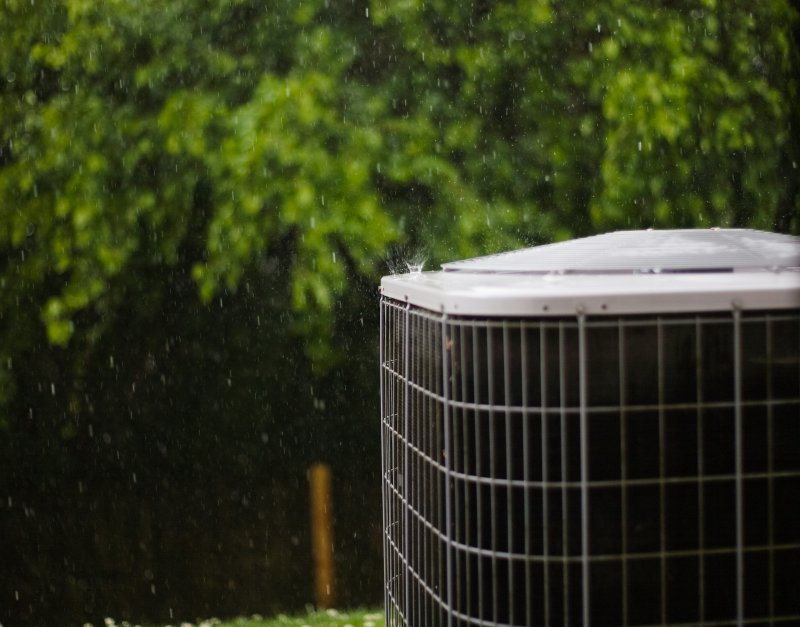 Outdoor air conditioning condenser unit beside a yard with green foliage