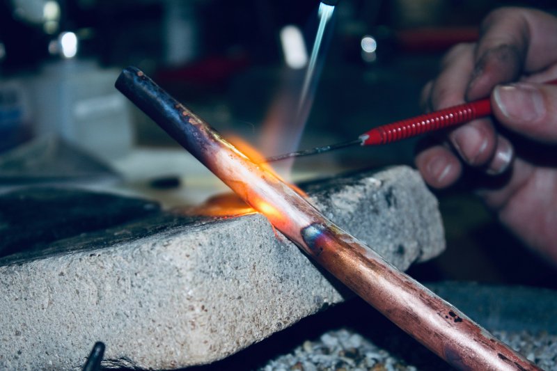 A torch heating a copper pipe to brazing temperature