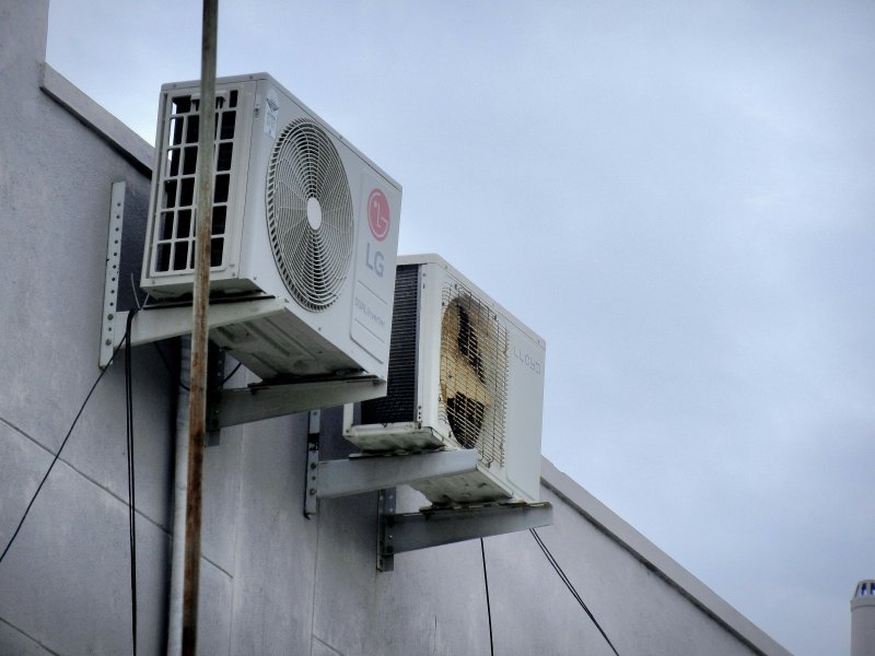 Two outdoor air conditioner condenser units mounted on the side of a residential building