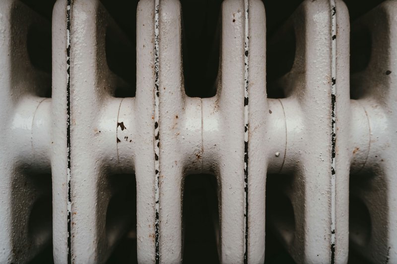 Close-up of a weathered cast-iron radiator with rust spots and peeling paint between the fins
