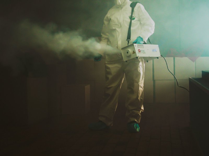 Operator in white hazmat suit running a fogging machine in a dim room