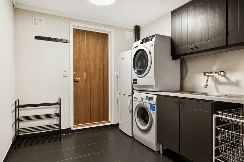 Residential utility room with stacked white front-loading dryer over washer, sink, and dark cabinetry