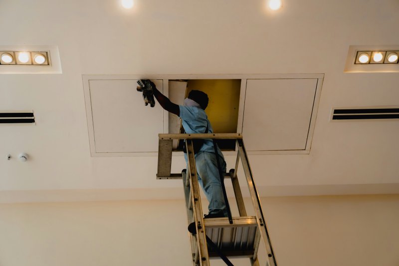 Service worker on a step ladder wiping the inside of a ceiling access panel