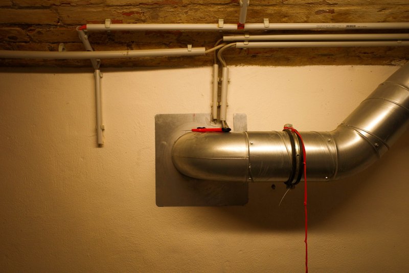 Rigid metal exhaust duct with elbow joint, secured by a clamp on a wall