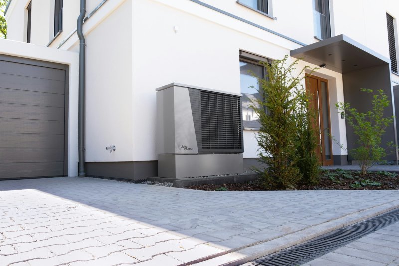 Modern residential home exterior with a gray garage, stone walkway, and a ductless mini-split outdoor condenser unit installed beside the house