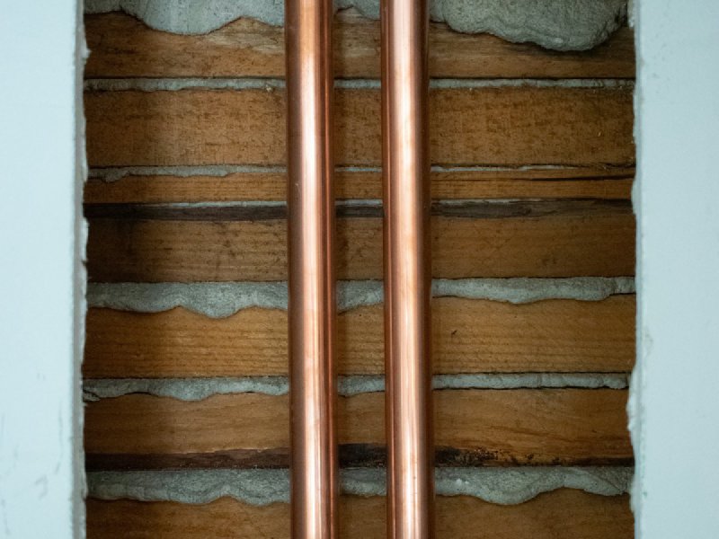 Two insulated copper refrigerant line set pipes running vertically through a wall cavity