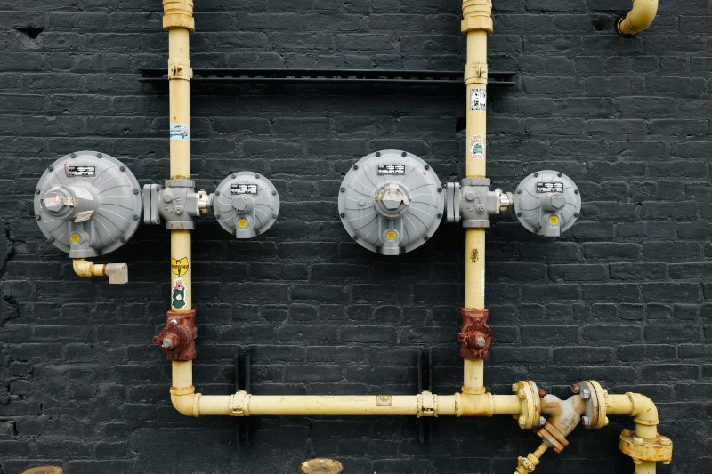Yellow gas service pipes and gray gas meters mounted on an exterior brick wall