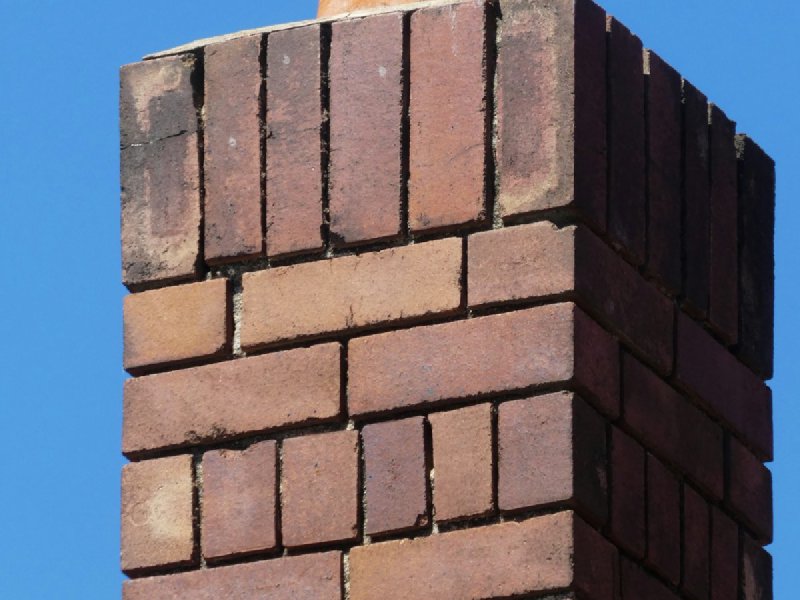 Red brick chimney with a cracked terracotta cap on a residential roof
