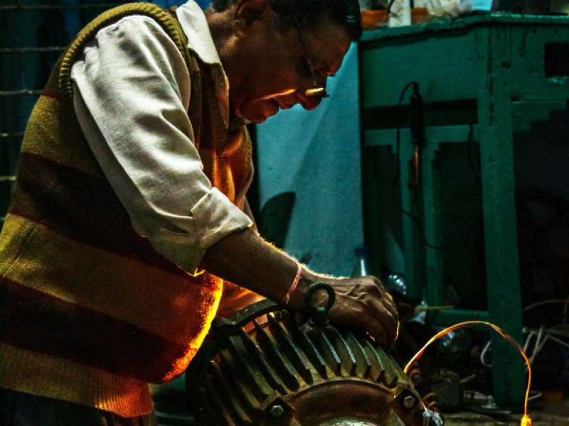 Technician using hand tools on a finned electric motor in a workshop with warm directional lighting