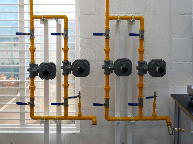 Yellow gas piping with shut-off valves labeled GAS NATURAL and GAS LP on a cinder-block wall