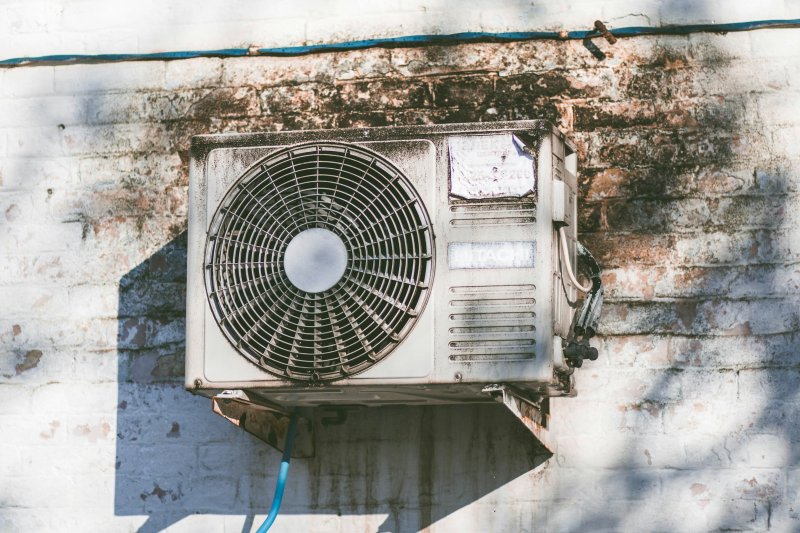 Weathered outdoor HVAC unit on a brick wall showing peeling paint and visible age