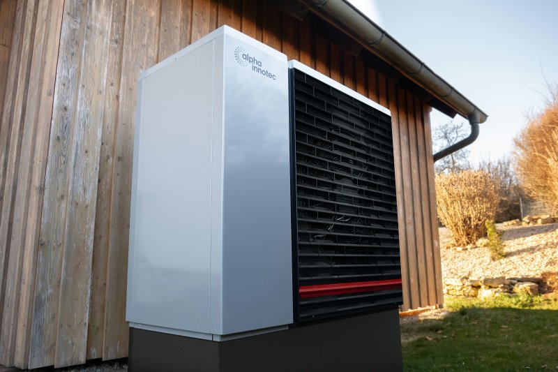 Residential heat pump outdoor unit mounted on the wood-clad exterior of a home