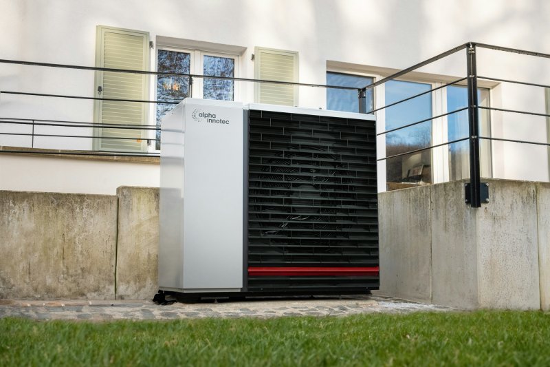 White and black residential heat pump unit installed on a stone patio next to a modern house