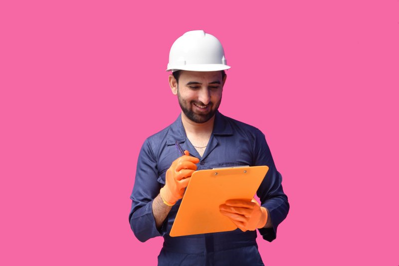 Construction worker in a hard hat and gloves writing on a clipboard