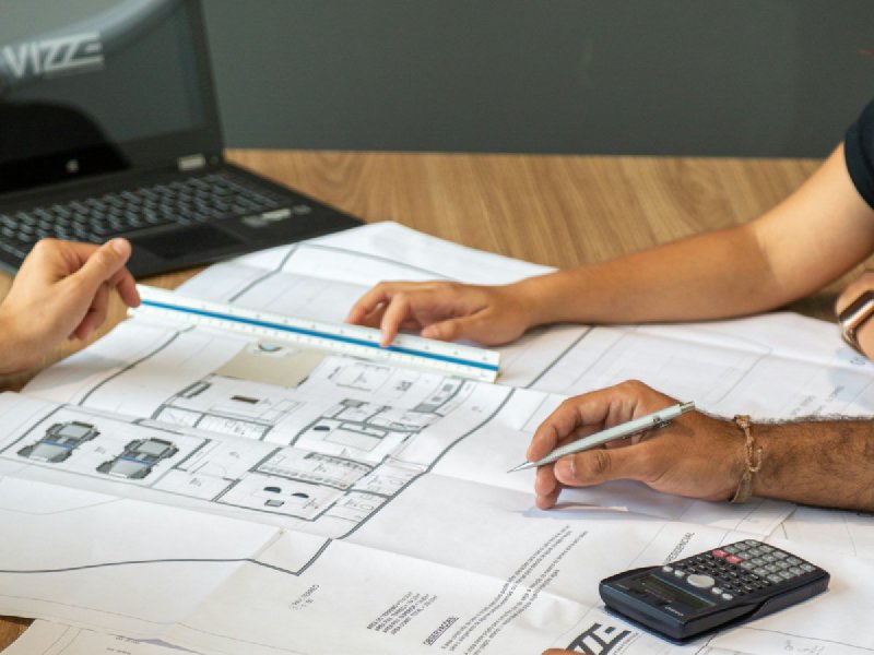 Two people reviewing architectural blueprints with drafting tools on a wooden desk