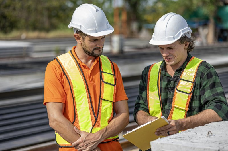 Two contractors in hard hats and safety vests reviewing project documents on a jobsite