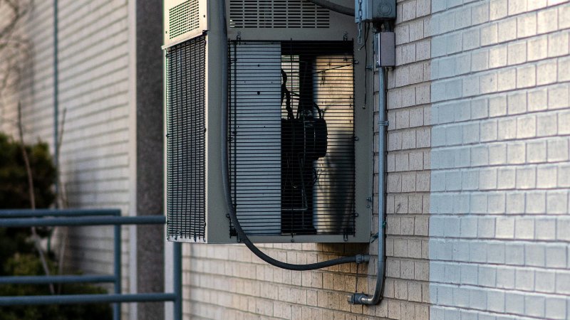 Outdoor HVAC condenser unit mounted on a brick building wall with refrigerant lines and electrical disconnect