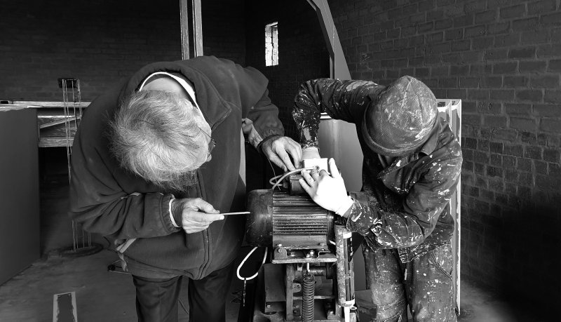 Two technicians repairing an electric motor in a brick-walled workshop