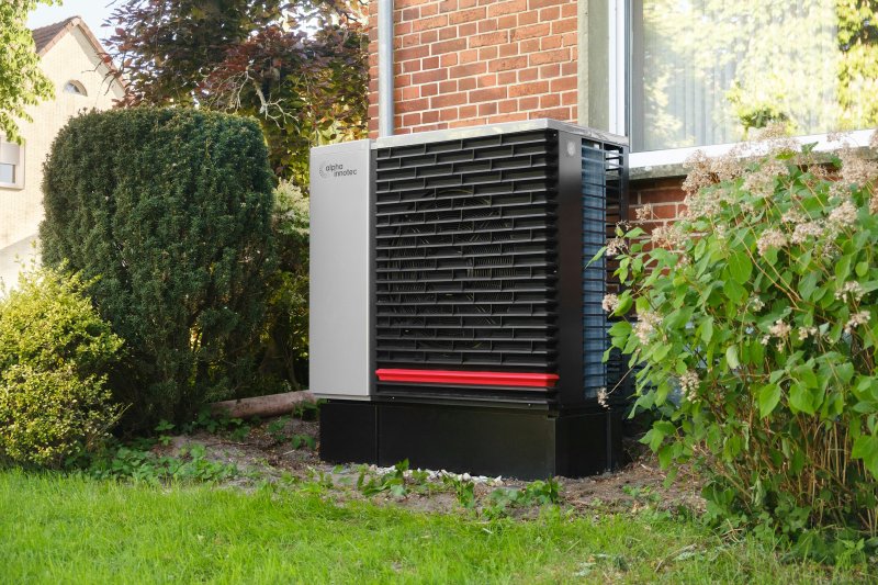 Gray and black residential outdoor air conditioning condenser unit beside a brick house