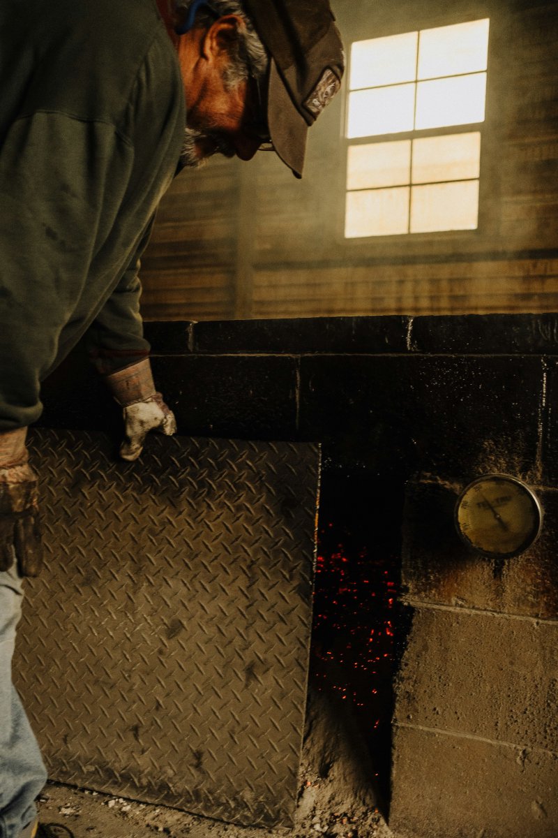 Technician in cap and gloves inspecting a heating unit with a mounted thermometer