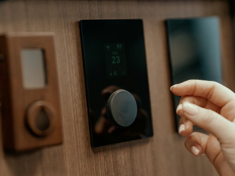 Hand adjusting a modern digital thermostat mounted on a wooden wall