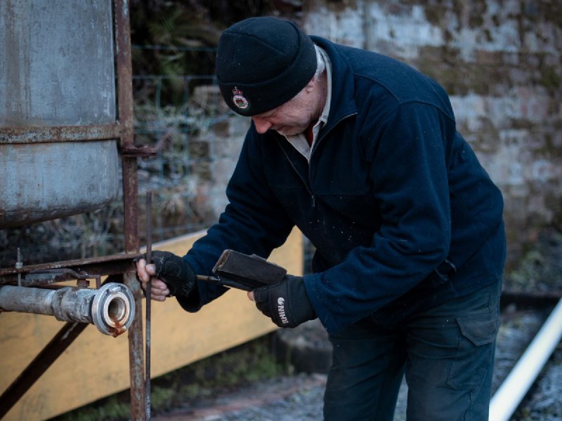 Plumber in dark workwear feeding a drain rod into a bucket while servicing a pipe