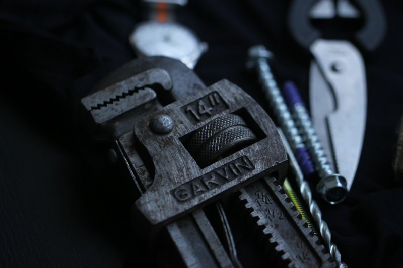 Worn 14-inch Garvin pipe wrench with other plumbing tools on a dark surface