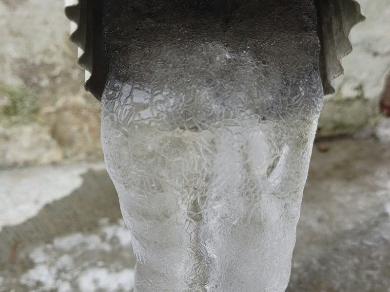 White supply pipe with water frozen into a cracked translucent column of ice