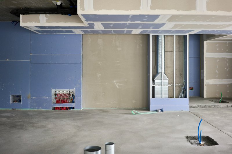 Construction interior showing a red plumbing manifold on the wall with multiple pipes feeding fixtures