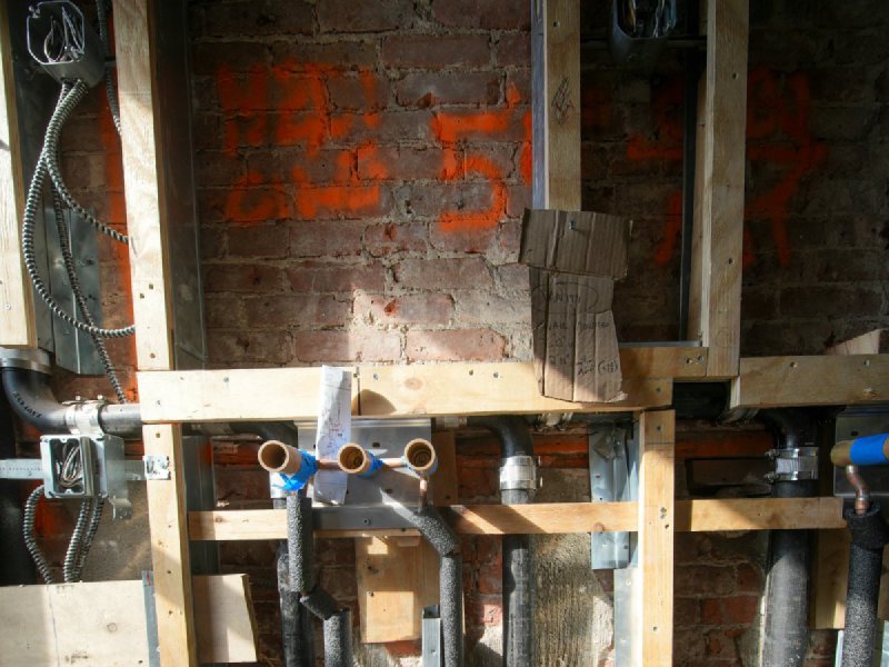 Exposed plumbing pipes and wooden framing inside an open wall during construction