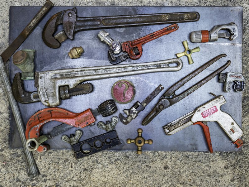 Repipe specialist tools laid out — pipe wrench, pipe cutter, and threader