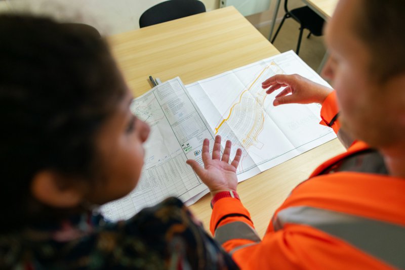 Two people reviewing construction blueprints on a wooden table — the contract-and-scope conversation that follows the camera scope on a sewer repair