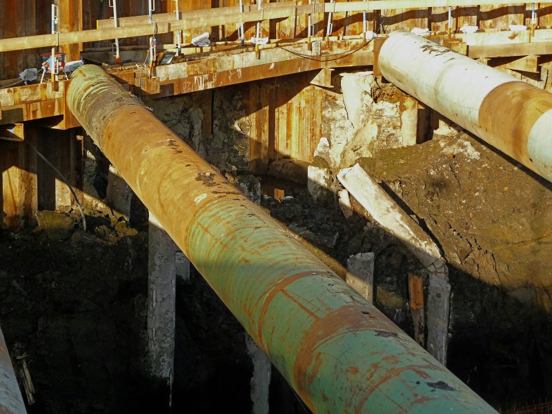 Two old rusted sewer pipes resting in a construction trench supported by wooden beams