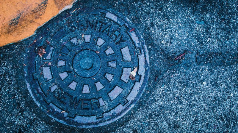 Blue municipal manhole cover stamped 'SANITARY SEWER' set into asphalt