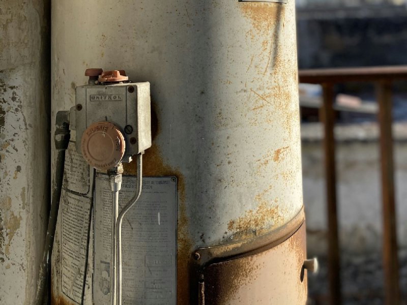 Cylindrical storage water heater tank with cold and hot supply pipes on a utility wall