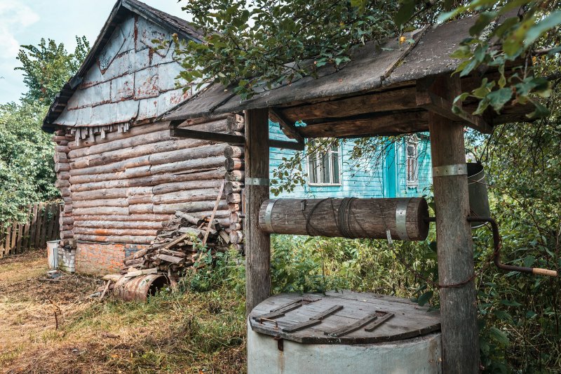 Weathered wooden well structure beside a rural log cabin