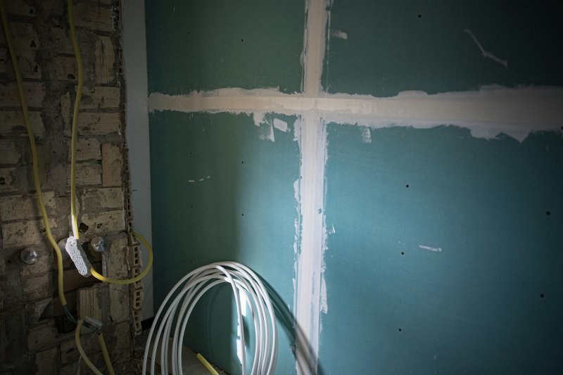 Green moisture-resistant drywall panels with taped seams and exposed electrical wiring on a basement wall
