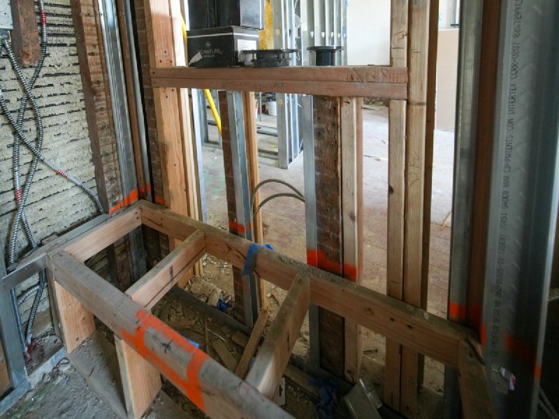 Wood-stud framing with metal corner studs and rough-in electrical wiring inside a basement under construction