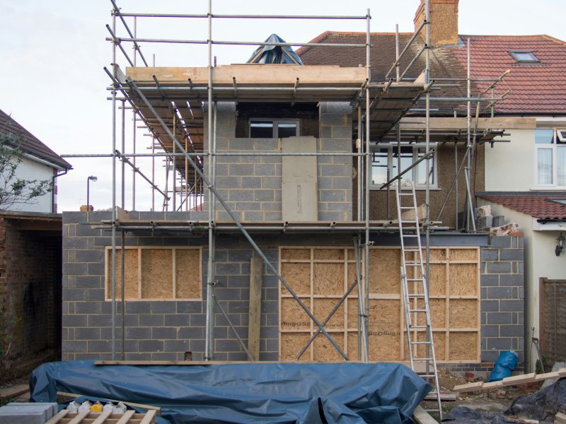 Two-story house wrapped in metal scaffolding during a vertical addition build