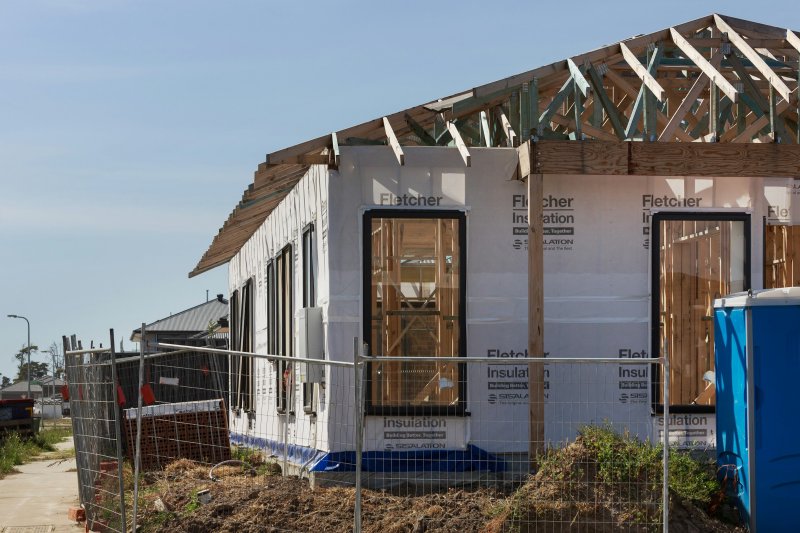 Single-story addition under construction showing exposed wooden wall framing, roof trusses, and white insulation panels