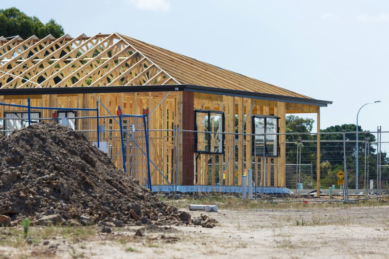 Framed weather-tight shell of a residential addition with wooden roof trusses and installed windows but no interior finish