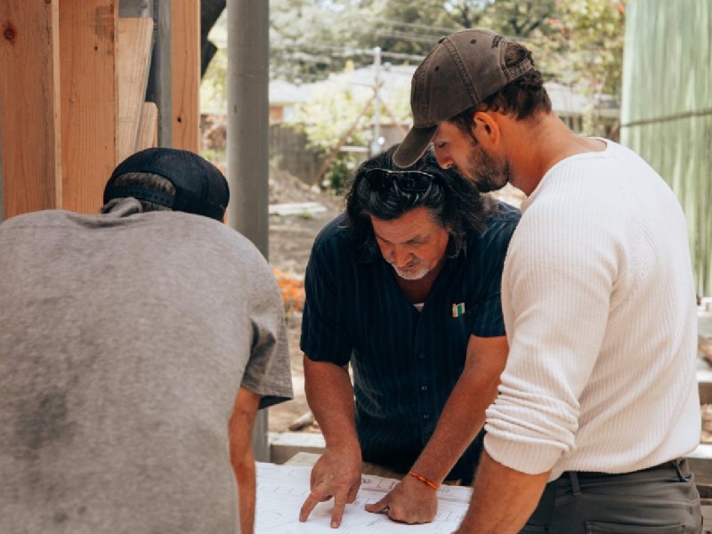 Three contractors in work clothes reviewing blueprints together at a residential job site