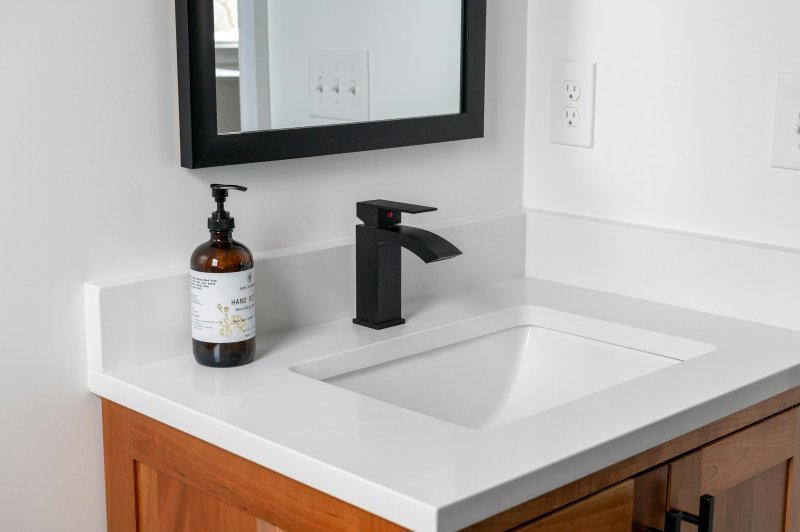 Modern bathroom vanity with black faucet on a white countertop and light wood cabinet