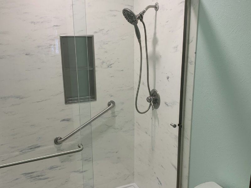 Walk-in shower with chrome grab bars, glass door, and handheld showerhead for accessibility