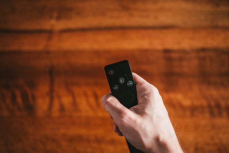 Hand holding a black remote control with a circular navigation pad and labeled buttons