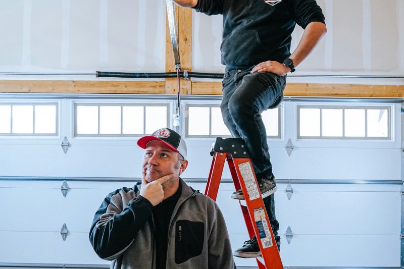Two installers mounting a ceiling-rail garage door opener in a new garage with the white sectional door visible behind them